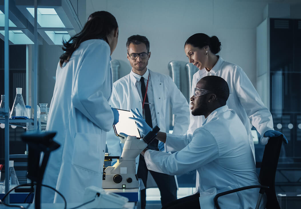 Scientists collaborate around a microscope, discussing cancer therapy treatment advancements.