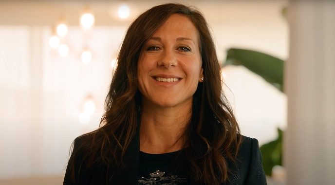 A woman with long hair smiles as she shares her experiences and stories in cancer care.