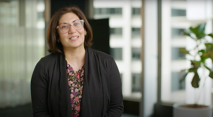Smiling woman in an office, discussing advancements in cancer care research, with cityscape in the background.