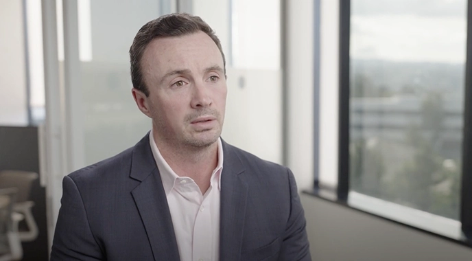 A man in a suit looks contemplative, possibly sharing insights on cancer care in a professional setting.