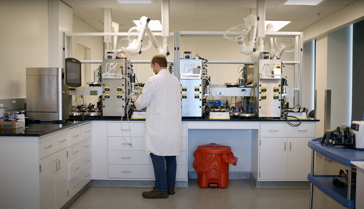 A scientist in a lab coat operates complex machinery, focused on cancer care research and innovation.