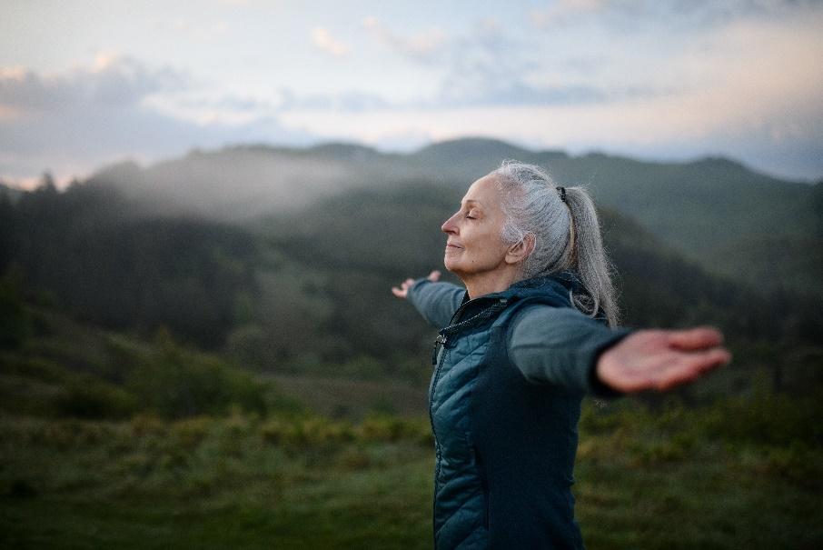 An elderly woman enjoys the outdoors, arms outstretched, embracing freedom and resilience, symbolizing her cancer care journey.