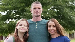 A family of three stands together outdoors, exuding unity and support, possibly sharing their cancer care journey.